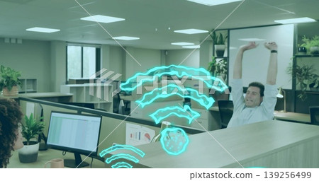 Floating turquoise wifi signals above coworkers working and stretching at dual monitors in office 139256499