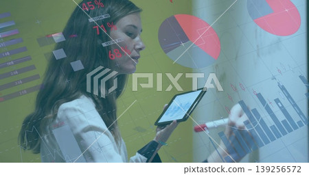 Business analyst writing chart on glass-board in meeting room, with tablet, red marker, copy space 139256572