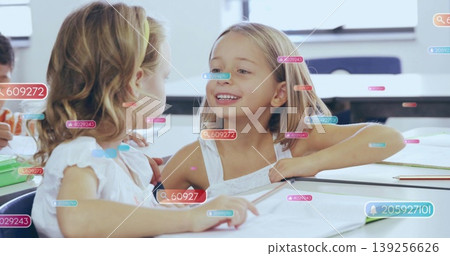 Leaning together, two child students sharing notes at classroom desks with notebooks, textbooks Leaning together, two child students sharing notes at classroom desks with notebooks, textbooks 139256626