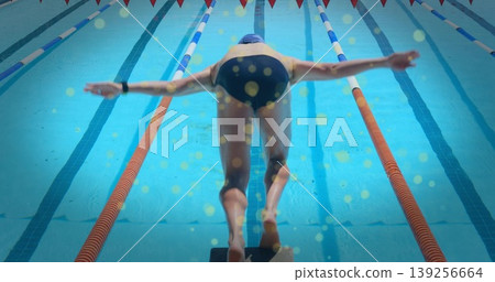 Adult male swimmer wearing cap and goggles bending, preparing to dive on starting block at pool Adult male swimmer wearing cap and goggles bending, preparing to dive on starting block at pool 139256664