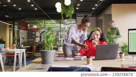 Collaborating two women colleagues sharing ideas at open plan office, with laptop and coffee cups Collaborating two women colleagues sharing ideas at open plan office, with laptop and coffee cups 139256678