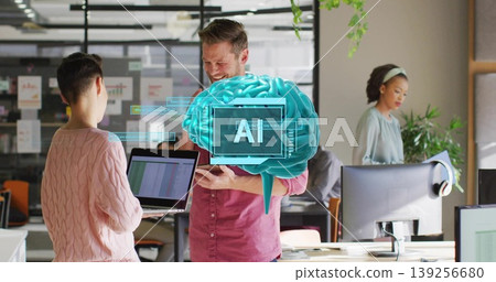 Discussing colleagues wearing business attire sharing laptop in open office, with AI brain graphic Discussing colleagues wearing business attire sharing laptop in open office, with AI brain graphic 139256680