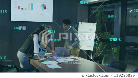 Coworkers analyzing charts with laptop around table in office, showing AR currency symbols 139256859