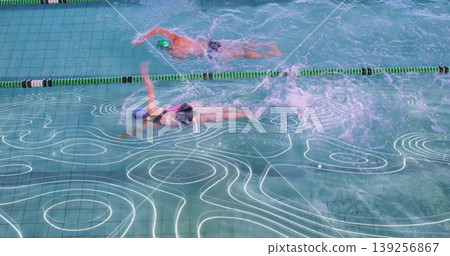 Swimming man and woman wearing swim caps and goggles training in lap pool, with lane divider Swimming man and woman wearing swim caps and goggles training in lap pool, with lane divider 139256867