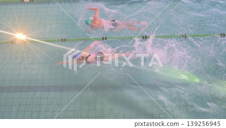 Swimming partners wearing swim caps, goggles stroking freestyle in lap pool with lane divider rope Swimming partners wearing swim caps, goggles stroking freestyle in lap pool with lane divider rope 139256945