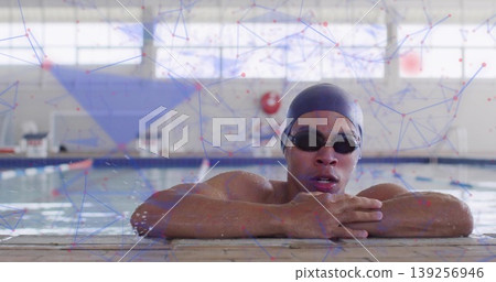 Leaning swimmer wearing swim cap, swim goggles on deck at pool, with lane ropes and lifebuoy 139256946