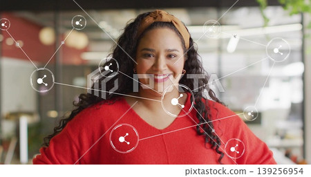 Mid-adult Hispanic woman wearing red sweater in modern open office, showcasing connection icons Mid-adult Hispanic woman wearing red sweater in modern open office, showcasing connection icons 139256954