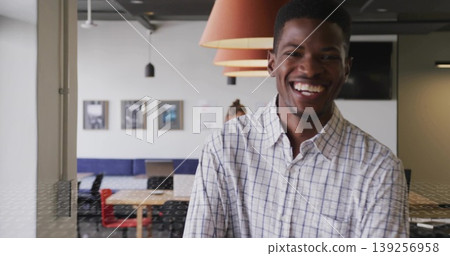Smiling checkered shirt man standing in office with furniture, lamps, photos, monitor, copy space 139256958