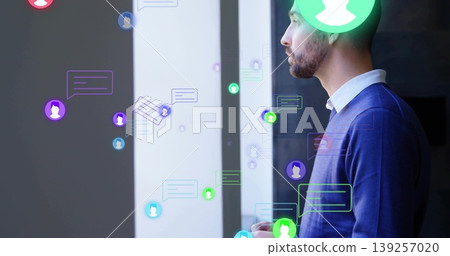 Gazing man wearing navy sweater through window at office with chat bubbles and icons, copy space Gazing man wearing navy sweater through window at office with chat bubbles and icons, copy space 139257020