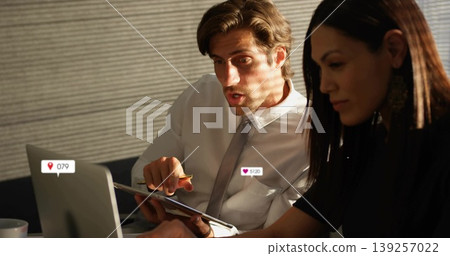 Pointing man and watching colleague discussing report on tablet at office meeting table with laptop Pointing man and watching colleague discussing report on tablet at office meeting table with laptop 139257022