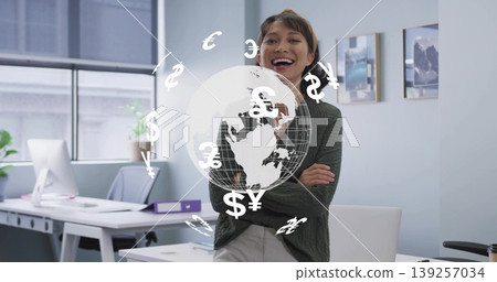Smiling Asian businesswoman leaning on desk in office, with holographic globe and currency symbols 139257034
