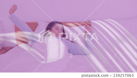 Stretching Indian woman wearing blue pajamas in bedroom with bed duvet pillows nightstand lamp 139257063