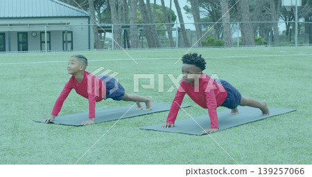 Holding plank pose two boys wearing red shirts and navy shorts on grass field, with mats Holding plank pose two boys wearing red shirts and navy shorts on grass field, with mats 139257066