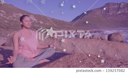 Indian woman meditating cross-legged on boulder, yoga mat, smartwatch and star overlays, copy space Indian woman meditating cross-legged on boulder, yoga mat, smartwatch and star overlays, copy space 139257082