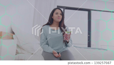Sitting Indian woman holding mint smoothie jar in modern bedroom, with nightstand and window 139257087
