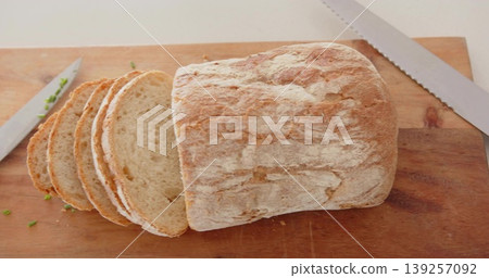 Displaying crusty artisan bread loaf sitting on wooden cutting board, with knives and herb bits Displaying crusty artisan bread loaf sitting on wooden cutting board, with knives and herb bits 139257092