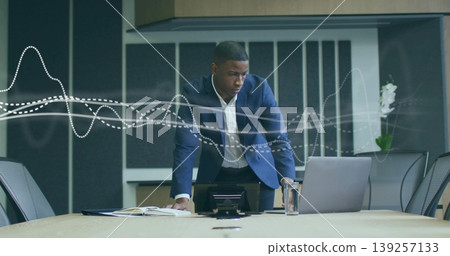 Leaning African American man reviewing data in boardroom with laptop, notebook, speakerphone, water Leaning African American man reviewing data in boardroom with laptop, notebook, speakerphone, water 139257133