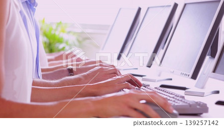 Office workers wearing polo shirts typing on keyboards at office desk, with monitors and plant Office workers wearing polo shirts typing on keyboards at office desk, with monitors and plant 139257142