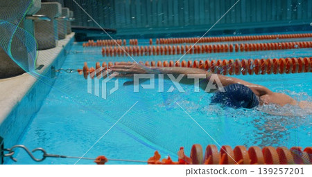 Swimming adult male performing front crawl in marked pool lane, with swim cap and orange dividers Swimming adult male performing front crawl in marked pool lane, with swim cap and orange dividers 139257201