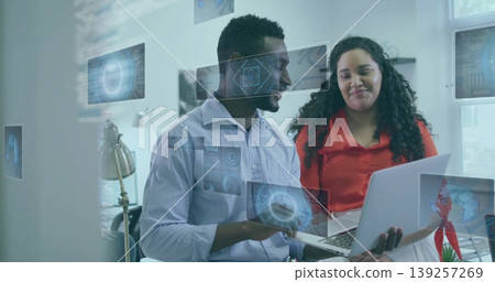 Two colleagues in button-up shirts collaborating in office, reviewing laptop with digital overlays Two colleagues in button-up shirts collaborating in office, reviewing laptop with digital overlays 139257269