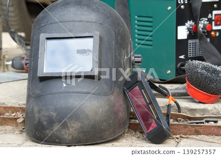Worn Welding Helmet and Auto-Darkening Goggles Beside Welding Machine and Wire Brush in Workshop Worn Welding Helmet and Auto-Darkening Goggles Beside Welding Machine and Wire Brush in Workshop 139257357