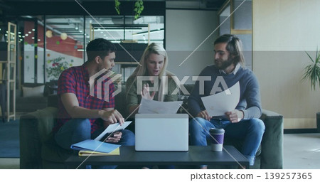 Collaborating three coworkers reviewing documents in office lounge, with laptop and coffee cup Collaborating three coworkers reviewing documents in office lounge, with laptop and coffee cup 139257365