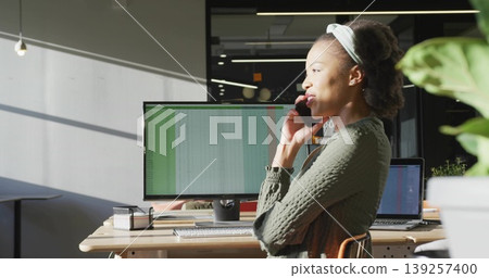 Leaning woman in green holding smartphone by desk, office, with monitor and laptop, copy space Leaning woman in green holding smartphone by desk, office, with monitor and laptop, copy space 139257400