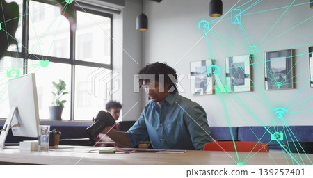 Holding DSLR camera, man in blue shirt sitting at office desk, with digital network overlay Holding DSLR camera, man in blue shirt sitting at office desk, with digital network overlay 139257401