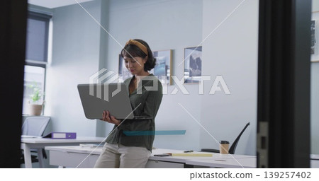 Leaning professional holding laptop over desk in office workspace, with smartphone and coffee cup 139257402