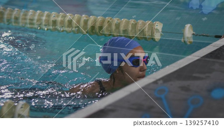 Swimmer gripping pool edge near floating lane rope at lap pool, with blue swim cap, goggles 139257410