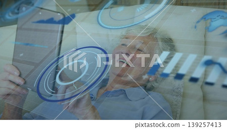Reclining senior woman in light blue shirt holding tablet computer at home, with interface overlays 139257413
