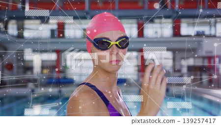 Standing female swimmer wearing pink swim cap and tinted goggles at lap pool, with digital overlay 139257417