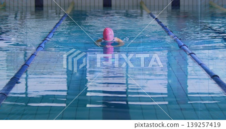 Swimming woman performing breaststroke in pool lane, with pink swim cap and blue lane dividers 139257419