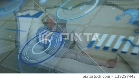 Reclining senior European woman holding tablet on chaise lounge, with floating hologram map overlay Reclining senior European woman holding tablet on chaise lounge, with floating hologram map overlay 139257442