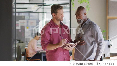 Discussing two office professionals holding notebook and pen in office with laptop and charts 139257454