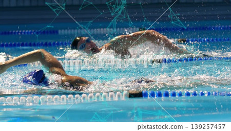 Two swimmers wearing caps and goggles racing in sports pool, with splashing water and divider ropes Two swimmers wearing caps and goggles racing in sports pool, with splashing water and divider ropes 139257457