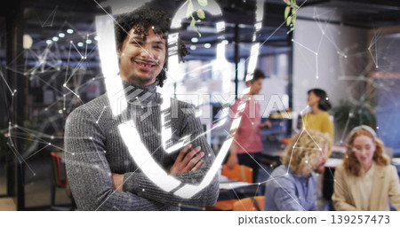 Posing man in sweater crossing arms and smiling at office, with laptops and digital network overlay Posing man in sweater crossing arms and smiling at office, with laptops and digital network overlay 139257473