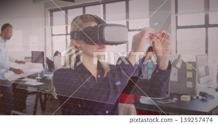 Woman wearing VR headset manipulating grid overlay in office, with scattered papers and monitors Woman wearing VR headset manipulating grid overlay in office, with scattered papers and monitors 139257474