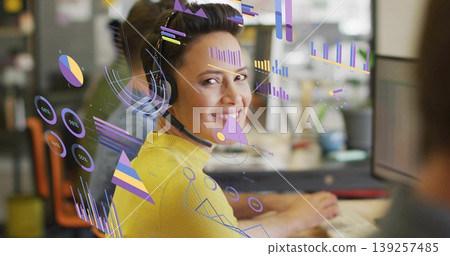 Showing agent in yellow sweater and headset turning toward camera at desk with charts, copy space Showing agent in yellow sweater and headset turning toward camera at desk with charts, copy space 139257485