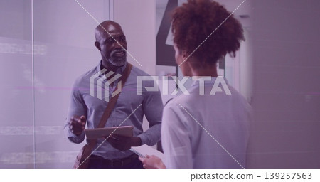 Gesturing two professionals discussing in office corridor, with tablet, notepad, pen and bag strap 139257563