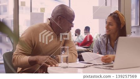 Senior man and Hispanic woman consulting documents at modern office with laptop and glass of water Senior man and Hispanic woman consulting documents at modern office with laptop and glass of water 139257569