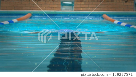 Gliding swimmer wearing swim trunks, cutting through lap pool water by orange-and-white lane ropes 139257571