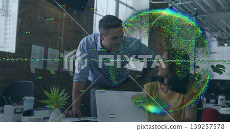 Leaning man in blue shirt and woman in yellow blouse collaborating at open-plan office, with laptop 139257578