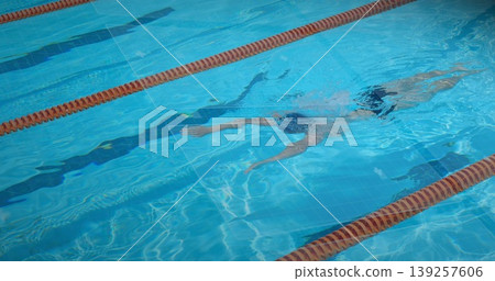 Gliding swimmer front crawling in outdoor pool, with swim cap goggles and orange lane divider ropes 139257606