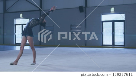 Arching skater leaning backward on ice rink, wearing skating dress and tights under overhead lights Arching skater leaning backward on ice rink, wearing skating dress and tights under overhead lights 139257611