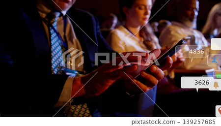 Tapping man in dark suit checking smartphone in dim conference auditorium with notification bubbles 139257685