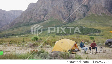 Campers sitting around fire pit in mountain campsite wearing warm jackets, with yellow tent and SUV Campers sitting around fire pit in mountain campsite wearing warm jackets, with yellow tent and SUV 139257722