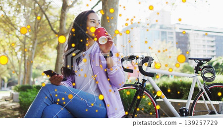 Asian woman holding red coffee cup to lips, checking smartphone on park bench with road bicycle 139257729