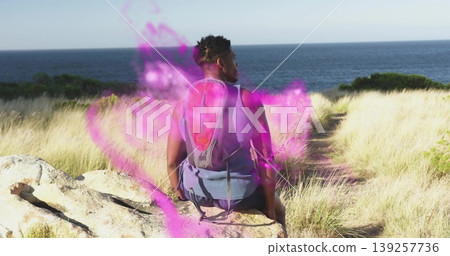 Sitting male hiker facing sea horizon on coastal bluff, with red-gray daypack and purple mist Sitting male hiker facing sea horizon on coastal bluff, with red-gray daypack and purple mist 139257736