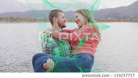 Man in plaid shirt carrying woman wearing pink sweater on rocky shore, with calm lake, mountains Man in plaid shirt carrying woman wearing pink sweater on rocky shore, with calm lake, mountains 139257737